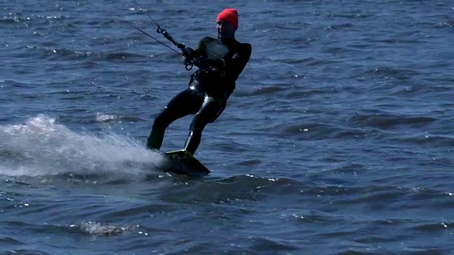慢镜头:一名男性风筝滑板者在河边的一块滑板上滑行。他在水上运动时做各种各样的运动。河水依然浑浊，冰刚刚融化。视频素材