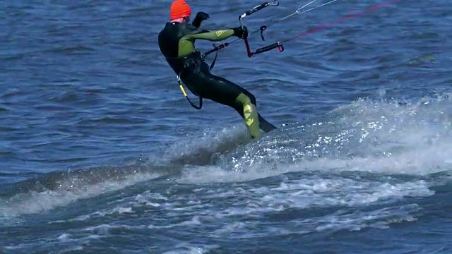 慢镜头:一名男性风筝滑板者在河边的一块滑板上滑行。他在水上运动时做各种各样的运动。河水依然浑浊，冰刚刚融化。视频素材