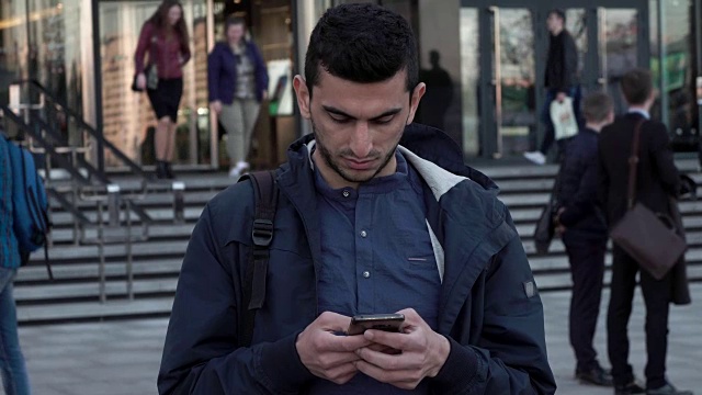 中东年轻人在城市中使用智能手机，人们走在后面视频下载