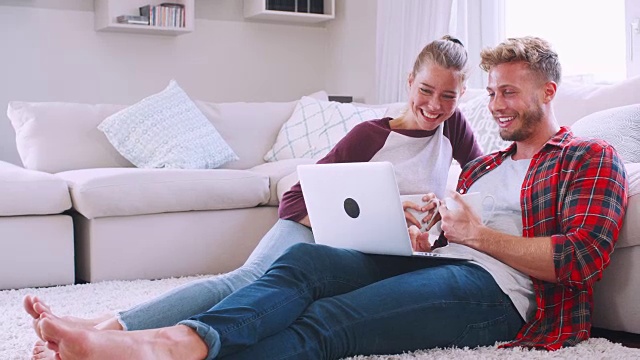一对年轻的白人夫妇坐在家里的地板上用笔记本电脑视频素材