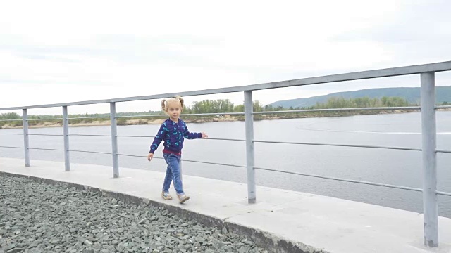 小女孩沿着篱笆跑和跳，背景是大河和山脉。视频素材