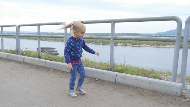 小女孩沿着篱笆跑和跳，背景是大河和山脉。视频素材