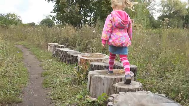 秋日里，小女孩在户外公园里踩着树桩和平衡行走。视频素材