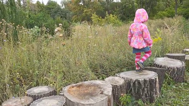 秋日里，小女孩在户外公园里踩着树桩和平衡行走。视频素材