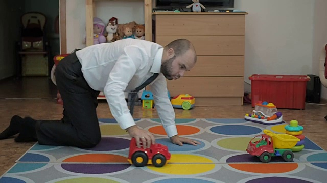 成年男性商人坐在婴儿室的地板上玩玩具车。视频下载