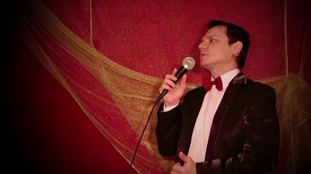 流行爵士歌手穿着燕尾服，打着蝴蝶领带，对着深红色背景的麦克风唱歌视频下载