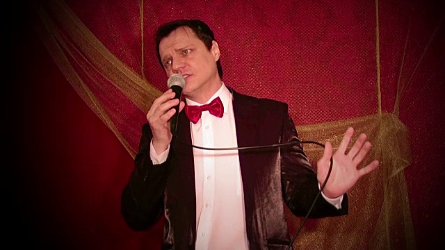 流行爵士歌手穿着燕尾服，打着蝴蝶领带，对着深红色背景的麦克风唱歌视频下载