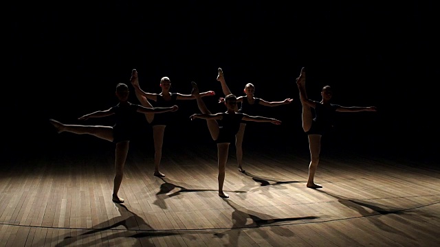 少女们在黑暗中在舞台上表演芭蕾舞。视频素材