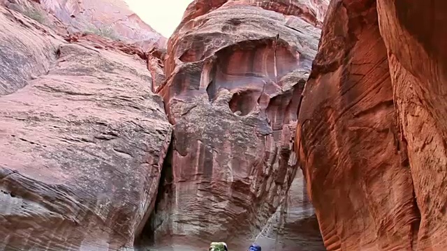 稳定的镜头拍摄的男人和女人徒步通过河流在深红色岩石沙漠狭缝峡谷。视频素材