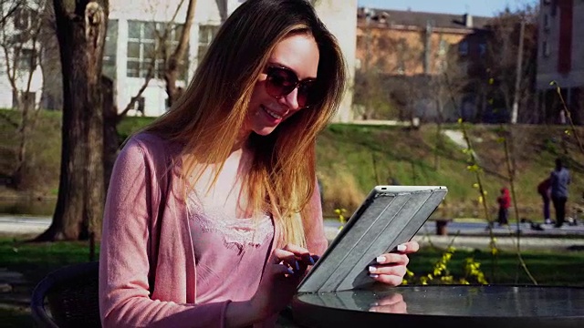 迷人的女孩在公园里用平板电脑工作，戴着墨镜休息视频下载