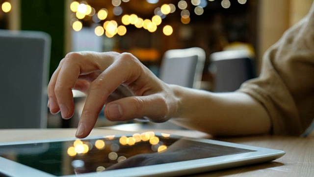 在一个模糊背景的特写镜头中，一个女人的手在用一个平板电脑视频素材