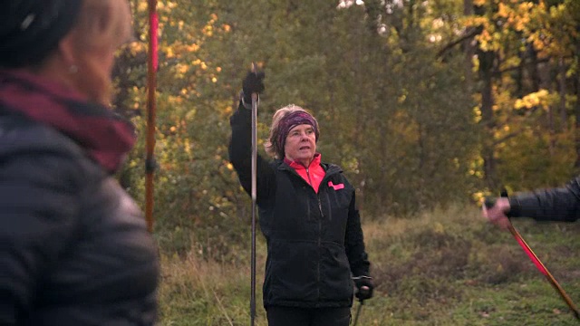 手持拍摄的男性和女性高级朋友热身与北欧的步行杆在球场上对着树视频素材