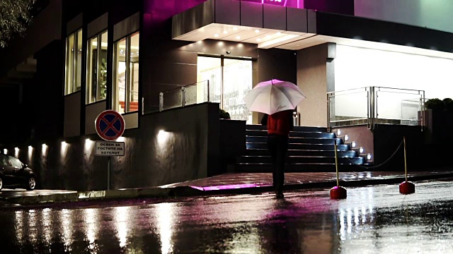 傍晚时分，女人在五颜六色的伞下朝大门走去视频下载