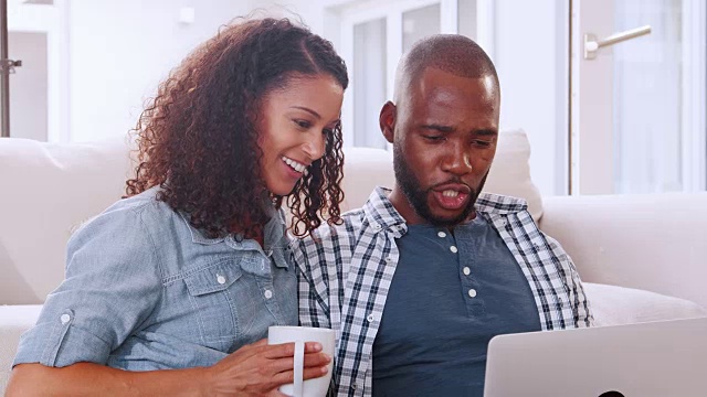 一对年轻的黑人夫妇坐在沙发上看电脑视频素材