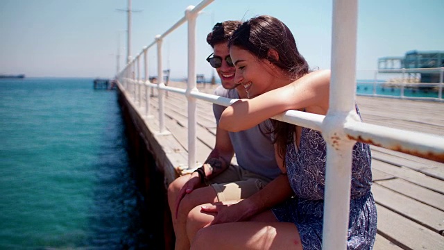 夏天，一对年轻夫妇坐在海边的防波堤上放松视频素材