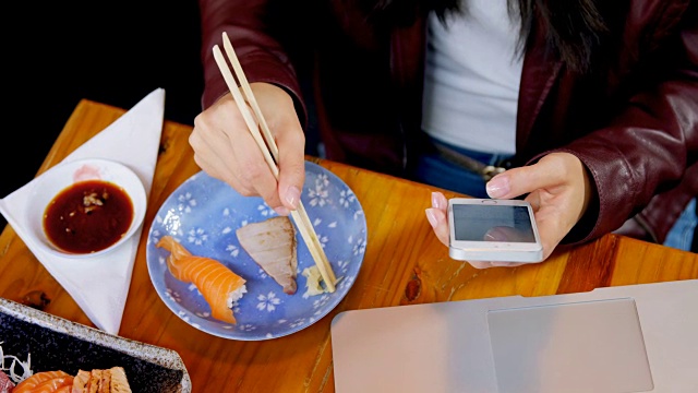 一个女人在4k餐厅边吃寿司边玩手机视频素材