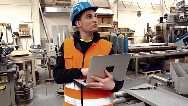 工业工程师戴安全帽穿安全外套使用笔记本电脑。他在重工业制造厂工作。视频素材