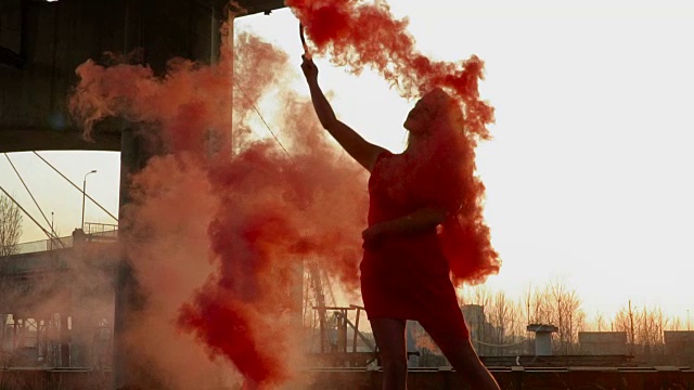 在废弃的桥旁，身着红裙的优雅女子与红烟共舞视频素材