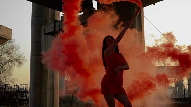 在废弃的桥附近，穿着红衣服的年轻女子与红烟跳舞视频素材
