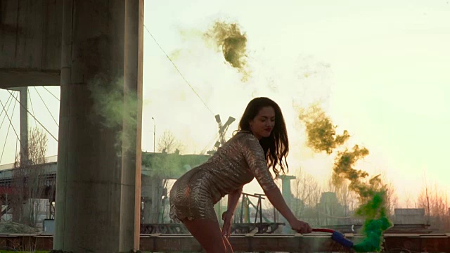 性感的女人穿着金色的裙子，在废弃的桥下与绿色的烟雾跳舞视频素材