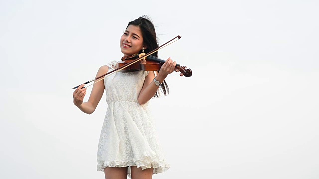 年轻美丽的亚洲女孩穿着裙子在海滩上拉小提琴视频下载