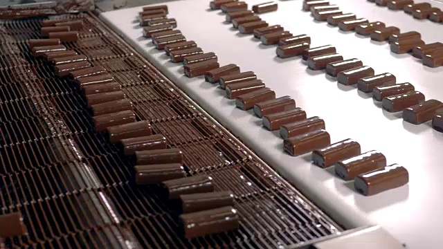 在一家食品厂，糖果在白色背景的传送带上移动。视频下载