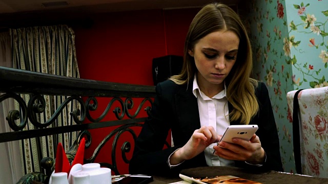 一个穿着商务套装的女孩坐在咖啡馆的一张桌子旁使用她的智能手机视频素材