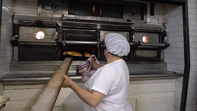 传统的意大利面包店。一位女面包师从烤箱里拿出热面包视频素材