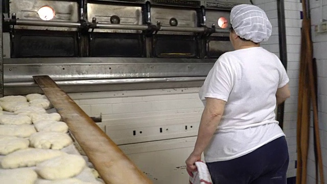 传统的意大利面包店。一位女面包师把热面包从烤箱中拿出来视频素材