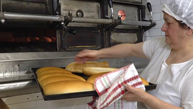 传统的意大利面包店。一位女面包师把热面包从烤箱中拿出来视频素材