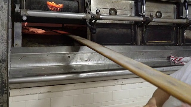 传统的意大利面包店。面包师用一块特制的长板把面包放进烤箱烘烤视频素材