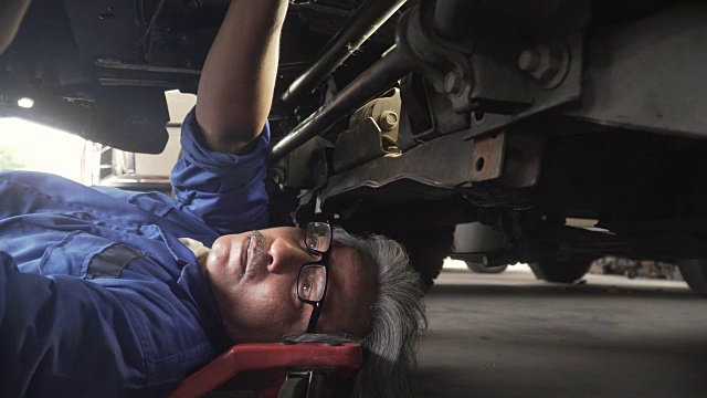 从车轮近侧视图:亚洲高级汽车技师在车辆下工作视频素材