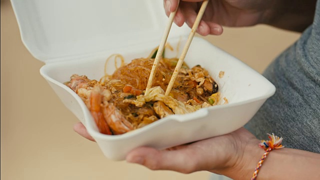 一个女人用筷子在外卖盒里吃亚洲炒面视频素材