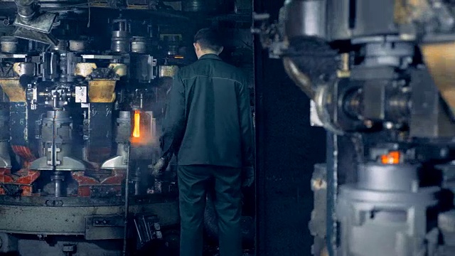 在工厂里，一名工人正在观看一种特殊的机器如何熔化瓶子。4 k。视频素材