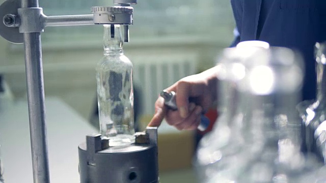 工厂工人检查瓶子，在一个特殊的仪器上旋转它。4 k。视频素材