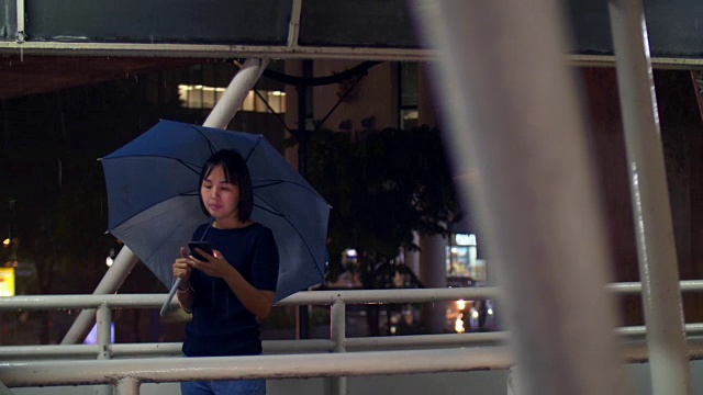 带着雨伞在雨中使用手机的女人视频素材