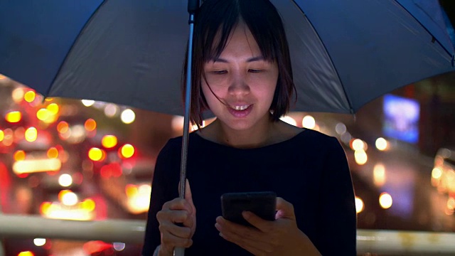带着雨伞在雨中使用手机的女人视频素材