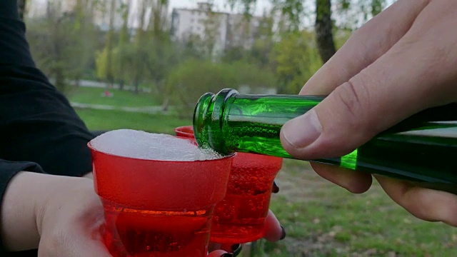 公园里有酒。男人的手在玻璃杯里倒香槟的特写。视频下载