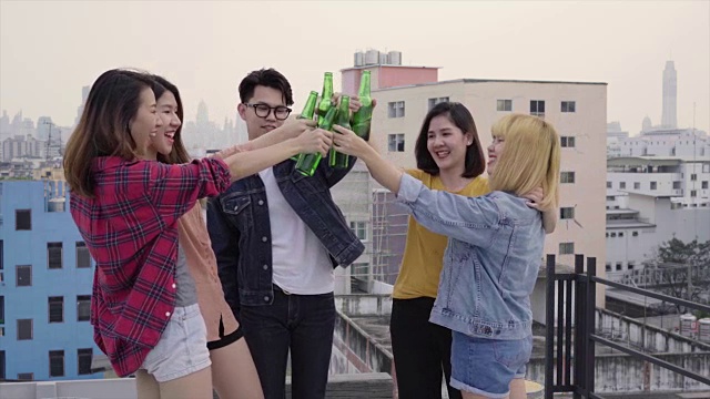 一群年轻的亚洲妇女和男子人们跳舞和举起他们的手臂在空中的音乐由dj在日落城市派对在屋顶上。年轻的亚洲女孩和男孩朋友一起喝酒视频素材