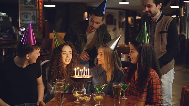 一名年轻女子在和朋友在咖啡馆庆祝节日时许了愿，吹灭了生日蛋糕上的蜡烛。快乐的人们笑着拍手。视频素材
