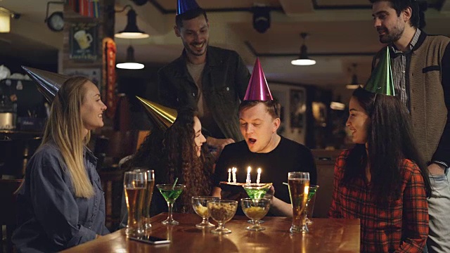 最好的朋友在年轻人的生日祝贺他，他吹灭了蛋糕上的蜡烛，感谢他的伙伴们举办了很棒的派对。有趣的节日与朋友的概念。视频下载