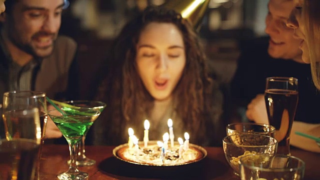 年轻漂亮的女人吹灭生日蛋糕上的蜡烛的特写镜头。快乐的人们笑着拍手。视频素材
