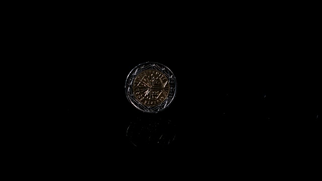 一枚两欧元硬币在反光表面上旋转的慢动作镜头。视频素材