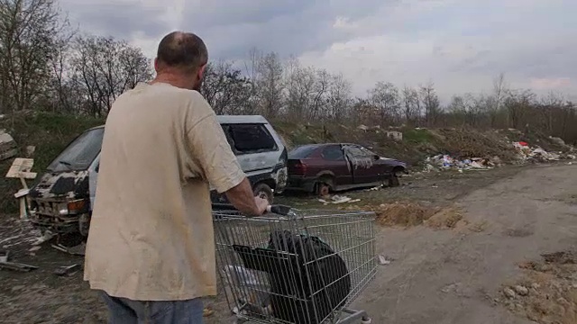 男性推着购物车在垃圾填埋场的后视图视频素材