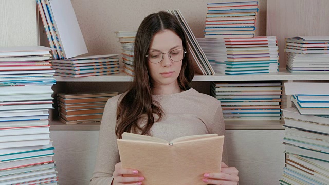 年轻的黑发女人戴着眼镜在看书。坐在书中视频素材