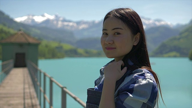 美丽和快乐的亚洲女孩享受她的一天在一个湖泊和山脉背景的高山景观步行桥视频素材