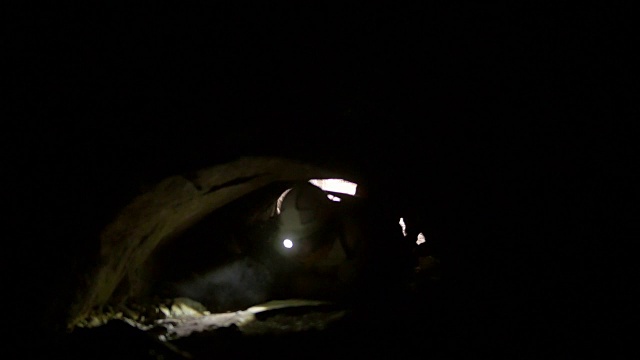 戴着头盔的年轻探险家四肢着地爬进黑暗的洞穴视频下载