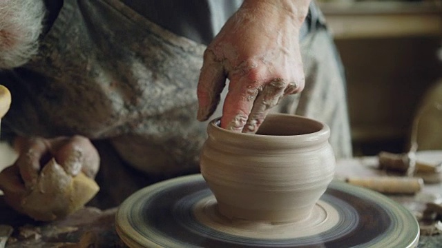专业的陶工是在陶轮上制作陶器，看着半成品的陶罐，检查工作的质量。传统职业与创造陶瓷理念。视频购买