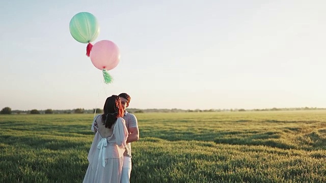 一对夫妇带着氦气球在苹果花园里散步，在日出时手拉手。慢动作拍摄视频素材