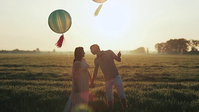 一对夫妇带着氦气球走进田野，在夕阳下亲吻视频素材